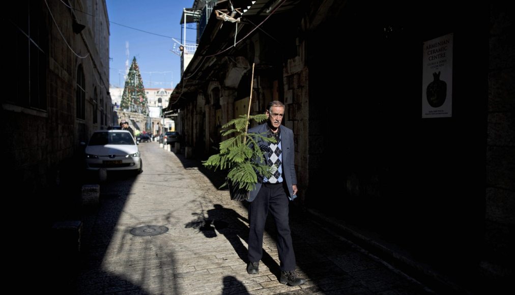 Un Palestinien portant un sapin de Noël dans une rue pavée de la vieille-ville de Jérusalem. Un Palestinien portant un sapin de Noël dans une rue pavée de la vieille-ville de Jérusalem. / Keystone/ Abir Sultan